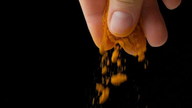 Hand pouring turmeric powder on black background, slow motion.