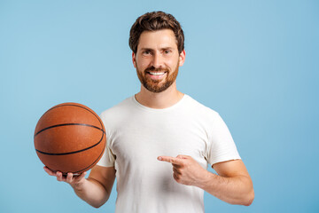 Smiling young man holding basketball ball pointing with hand and finger