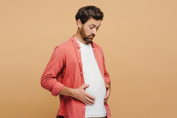Upset young man having stomachache, isolated on beige background
