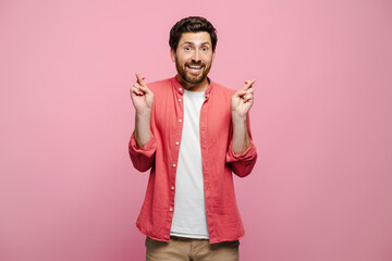 Young Caucasian man isolated on pink background crossing fingers for luck