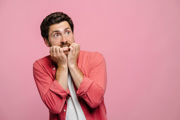 Shocked scared young Caucasian man with hands covering mouth on pink background