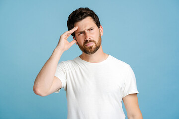 Portrait of young man looking stressed while having headache, over blue background