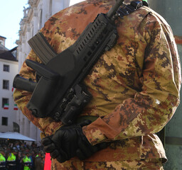 Army soldier in camouflage uniform with gloves and assault rifle monitoring crowd in city square