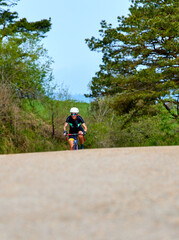 A woman cyclist training on a lonely road on a sunny day wearing a black jersey and bib shorts and...