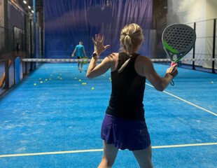  A woman is playing padel, hitting a ball on a bright blue court, 