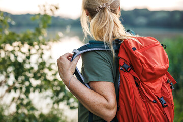 Naklejka premium Woman hiker puts on red backpack during hike in nature