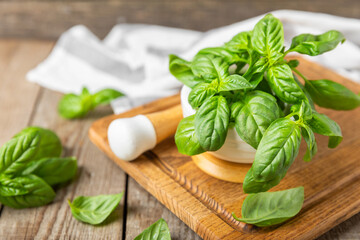 Fresh green basil in a mortar on a textured wooden background. Organic spices and herbs. Vegan. Fresh kitchen herbs. Fresh basil being made into pesto with mortar and pestle.Copy space. Place for text