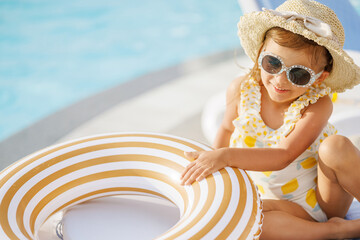 Cute little toddler girl in a hat and sunglasses relaxing on inflatable toy ring floating in pool...