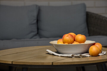 Bowl of fresh apricots on wooden table with sofa in background