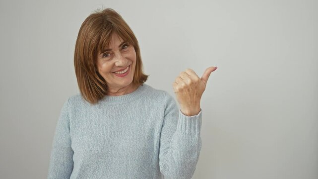 Cheerful middle age woman with short hair, confidently standing and boldly showing a thumbs-up, while wearing a comfy sweater and pointing to the side. isolated on a sparkling white background.