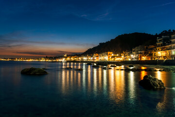 night town coast with flashlights from embarkment and reflection in sea gulf water with golden urbal lights and blue hour sky on background of landscape