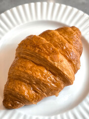 Freshly baked croissant on a white plate on a grey background. Minimal composition