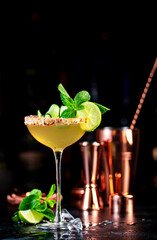 Spicy margarita summer cocktail drink with silver tequila, lime juice, syrup, mint and ice in glass with salted pepper rim, dark background