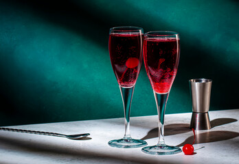 Red alcoholic cocktail drink with black currant liqueur, sparkling wine and cherry. Dark green background