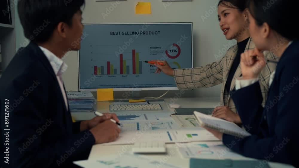 Poster colleagues analyze sales data, focusing on graphs and charts during a business meeting in a modern o