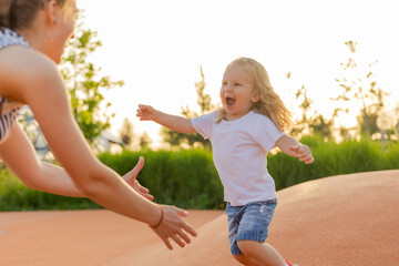 Cute blonde kid with curly hair walks in the playground in summer