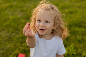 Cute blonde kid with curly hair walks on the lawn with soap bubbles in summer