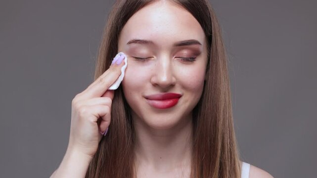 A young beautiful girl removes makeup with a cotton pad and micellar water from her face and eyes.