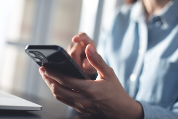 Close up, business woman using mobile smart phone searching the information, surfing the internet during working on laptop computer at office, social media marketing