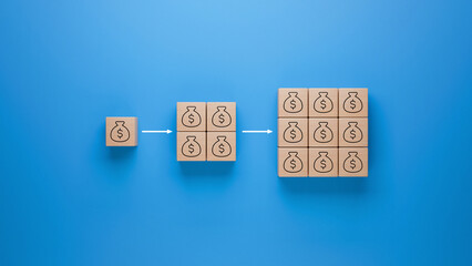 Wooden blocks with money bag icon on blue background, increasing wealth represented by multiplying blocks, financial growth and economic success in business investment concept