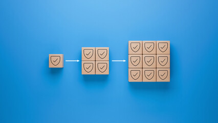 Wooden blocks with shield checkmark icon on blue background, security and protection multiplication represented by increasing blocks, cybersecurity and safety assurance concept
