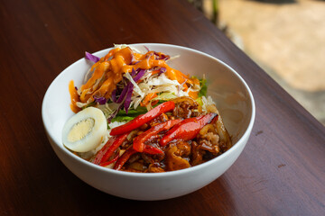 spicy blackpepper rice bowl, served with boiled egg, chili, and salad, on a white bowl, over wooden table