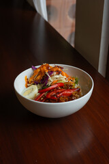 spicy blackpepper rice bowl, served with boiled egg, chili, and salad, on a white bowl, over wooden table