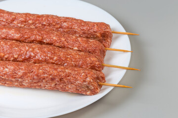 Raw lula kebab on wooden skewers on dish, close-up