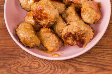 Prepared meat patties in bowl on rustic table close-up