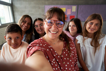 Elementary school teacher taking a cheerful selfie with her students in classroom.