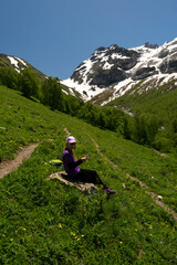 Fototapeta premium Girl with hat and backpack resting on rock in alpine scenery.