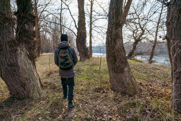 A teenage boy walking along the riverbank and forest, early spring landscape, the concept of hiking and outdoor activities