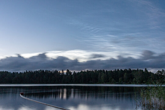 charming night landscape with silver clouds, silver clouds over the lake, dark forest silhouette in the background, mesospheric clouds