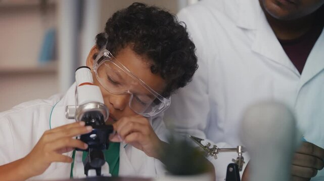 African American boy looks at lab sample under microscope, father supervises