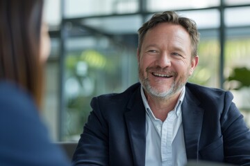Fototapeta premium A cheerful individual in a dark blue suit is smiling warmly during a conversation in an office environment, capturing the essence of professional friendliness and approachability.