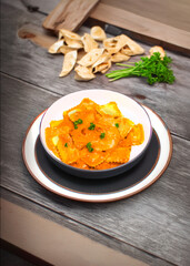 A delectable bowl of butternut squash ravioli in creamy sauce, garnished with fresh parsley. The rustic background includes bread crisps and a sprig of fresh parsley, enhancing the culinary appeal.