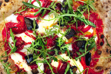 Close-up of a delicious vegetarian gourmet pizza topped with fresh arugula and an assortment of roasted vegetables, including peppers, eggplant, on a crispy crust. Ideal for food and culinary themes/