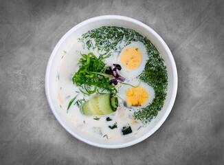 Cold Okroshka Soup with Eggs, Vegetables, Meat, Herbs and Kefir. Top view, on a gray background.