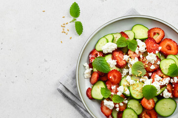 Healthy cucumber strawberry feta cheese salad with honey lemon dressing on plate. Top view, flat lay, copy space.