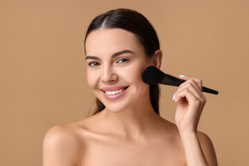 Fototapeta premium Smiling woman applying makeup with brush on beige background