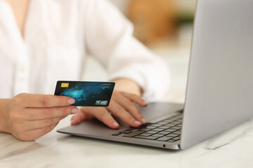 Online banking. Woman with credit card and laptop paying purchase at white marble table, closeup