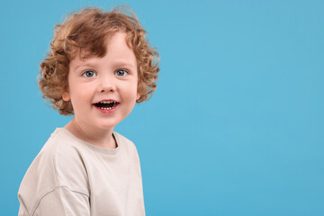 Portrait of cute little boy on light blue background, space for text