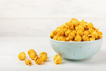 Sweet caramel popcorn in a bowl on a wooden background. Salted caramel popcorn. Caramel sauce. Close up. Topping. Place for text. Copy space