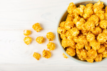 Sweet caramel popcorn in a bowl on a wooden background. Salted caramel popcorn. Caramel sauce. Close up. Topping. Place for text. Copy space