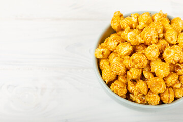 Sweet caramel popcorn in a bowl on a wooden background. Salted caramel popcorn. Caramel sauce. Close up. Topping. Place for text. Copy space