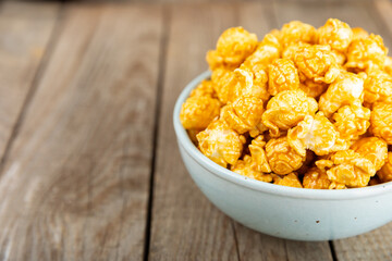 Sweet caramel popcorn in a bowl on a wooden background. Salted caramel popcorn. Caramel sauce. Close up. Topping. Place for text. Copy space