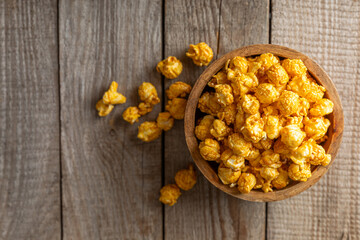 Fototapeta premium Sweet caramel popcorn in a bowl on a wooden background. Salted caramel popcorn. Caramel sauce. Close up. Topping. Place for text. Copy space