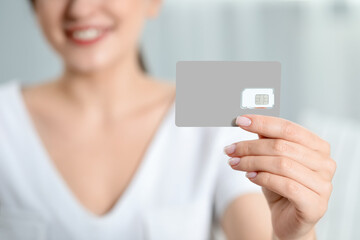Woman holding SIM card at home, closeup