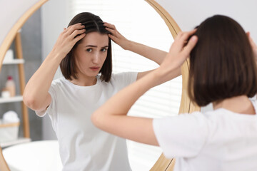 Fototapeta premium Sad woman with hair loss problem looking at mirror indoors
