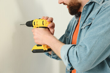 Smiling man drilling white wall at home, closeup